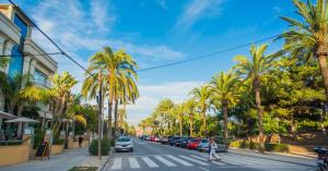 a street with palm trees and a person crossing a crosswalk at Beach Lovers' Paradise, bright apartment for 2/3 in Vilanova i la Geltrú