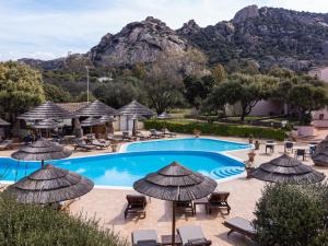 a pool with chairs and umbrellas and a mountain at Hotel Airone in Baja Sardinia