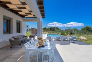 einen weißen Tisch und Stühle auf einer Terrasse mit einem Pool in der Unterkunft Panaxia Villas in Theologos