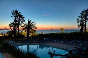a swimming pool with palm trees and a sunset at Hôtel La Nartelle in Sainte-Maxime