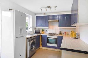 eine Küche mit blauen Schränken und einem weißen Kühlschrank in der Unterkunft The Nora - 4 Bed in Thamesmead