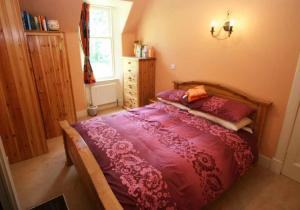 a bedroom with a bed with a purple comforter and a window at Cluny Mains in Newtonmore