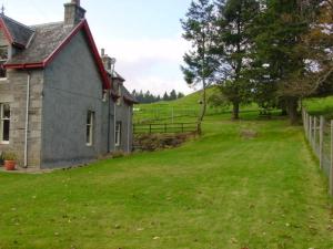 an old house on a green field with a fence at Cluny Mains in Newtonmore
