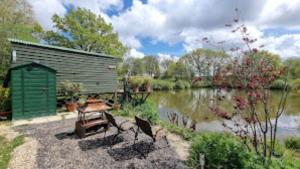 ein Picknicktisch und eine Bank neben einem See in der Unterkunft Snug & Secluded Lakeside Shepherds Hut 'Carp' in Uckfield