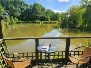 a table and chairs on a balcony with a view of a river at Snug & Secluded Lakeside Shepherds Hut 'Carp' in Uckfield