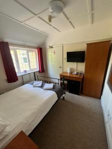 a bedroom with a bed and a desk with a television at The Admirals Inn Guest House in Bracknell
