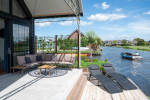 een patio met een bank en stoelen naast een rivier bij 4 to 6 persons waterfront villa in Roelofarendsveen