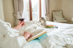 een vrouw in bed met een boek en een glas wijn bij Castello Bonaria Wine & Spa Resort in Campiglia Marittima