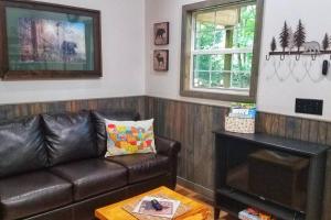 a living room with a leather couch and two windows at Holly Nest a Cozy Cabin Getaway near Gatlinburg in Cosby