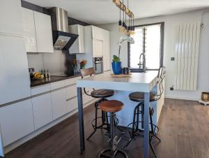 una cocina con armarios blancos y una isla con taburetes en Maison BALARUC LES BAINS, en Balaruc-les-Bains