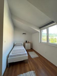 a white bedroom with a bed and a window at Apartments Majić in Kaštela