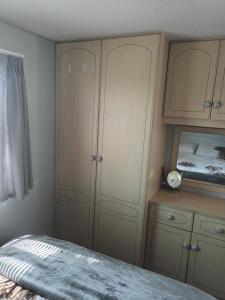 a bedroom with wooden cabinets and a bed with a clock at Carn Kenidjack View Caravan, space, peace and tranquillity in Penzance