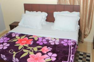 a bed with a purple and white blanket and pillows at Alice Gardens & Campsite in Entebbe