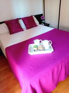 Una cama con una manta rosa y dos tazas. en Acogedor apartamento con piscina y garaje, en Huesca