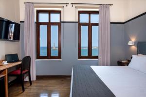 a hotel room with a bed and a desk and windows at Mosaic Venetian Harbour Suites in Chania