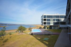 a building with a swimming pool next to a body of water at Gran Depto 2dorm Los Molinos PREVIAJE in Villa General Belgrano