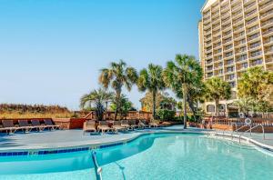 einen Pool mit Stühlen und Palmen sowie ein Gebäude in der Unterkunft Beach Cove Resort in Myrtle Beach