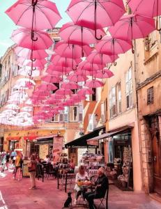 Um monte de guarda-chuvas cor-de-rosa pendurados numa rua. em Appartement 2 Pièces à 5 Minutes des Musées em Grasse