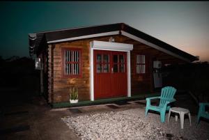 Cabaña de madera pequeña con puerta roja y 2 sillas en Chalets Boiskanon B en Matoury