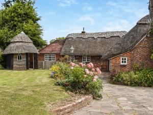 an old brick house with a thatched roof and flowers at The Old Thatch in Hailsham