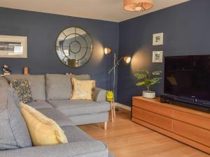 a living room with a gray couch and a television at Bluebell Barn in Grampound