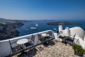 Un balcón con mesas y sillas y vistas al océano. en Eteoro Suites en Imerovigli