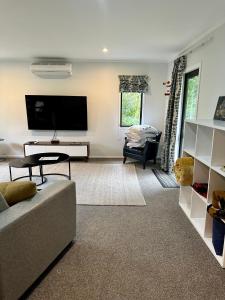 a living room with a couch and a flat screen tv at Peaceful cottage in beautiful landscaped native bush gully in Tamahere