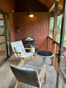 a porch with chairs and a table and a grill at Peaceful cottage in beautiful landscaped native bush gully in Tamahere