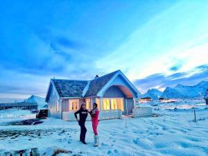 two people standing in the snow in front of a house at BanPim Beachside Lofoten in Ramberg