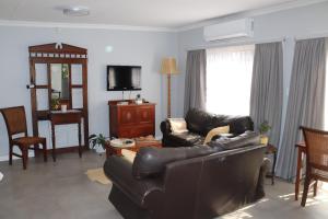 ein Wohnzimmer mit einem Ledersofa und einem TV in der Unterkunft Giraffe's Rest, Self Catering Studio Apartment in White River