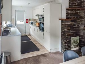 une cuisine avec des placards blancs et un mur en briques dans l'établissement Valley Truckle Bungalow, à Camelford