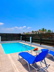 duas cadeiras azuis e uma mesa ao lado de uma piscina em 3 Bedroom Coral Bay Beach Seaview Villa I Private Pool em Pegeia ou Pegya