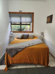 a bedroom with a bed with an orange blanket and a window at Santika Sunhill Cottage in Stellenbosch