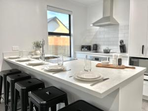 a kitchen with a counter with stools and plates and a sink at Brand New & Ready for You! By KOSH BNB in Hamilton +14 photos