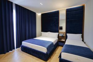 two beds in a small room with blue curtains at Duka's Hotel in Ksamil