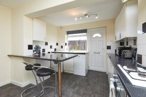 cocina con armarios blancos y encimera negra en Comfortable 4-Bed House in Hucknall Nottingham, en Nottingham