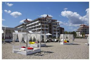 a group of white beds on a beach with a building at Aparthotel Regina Mare in Tsarevo