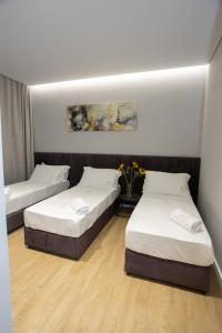 two beds in a room with white walls and wood floors at Bee Hotel in Vlorë