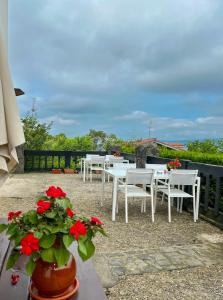 un patio con mesas blancas y flores rojas en Agroturismo Kostegi en Urnieta
