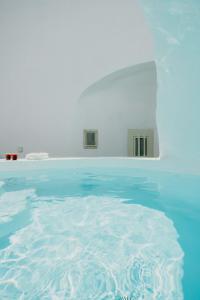 une piscine d'eau bleue et un bâtiment blanc dans l'établissement Villa Patitiri cave house with private pool in Megalochori Santorini, à Megalochori