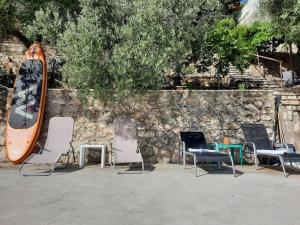 a group of chairs and a surfboard sitting next to a stone wall at Mystica - charming studio apartment on the beach in Kruševo