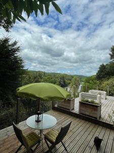 a table and chairs on a deck with a green umbrella at Le Relais des galets in Domme