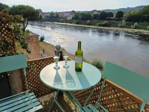 butelkę wina i dwa kieliszki na stole obok rzeki w obiekcie The Riverview Loft w mieście Sainte-Foy-la-Grande