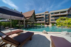 a swimming pool with chairs and an umbrella next to a building at Maikhao Palm Beach Resort - SHA Plus in Mai Khao Beach