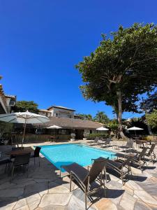 - une piscine avec des chaises, des parasols et un arbre dans l'établissement Pousada Corsario Buzios, à Búzios