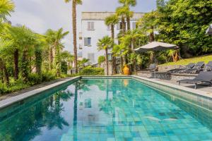 a swimming pool with palm trees and a white building at Villa Magnolia - Boutique Superior Rooms in Locarno