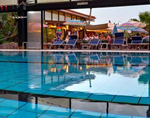 a swimming pool with people sitting in chairs and umbrellas at Green Sporting Club Hotel in Alghero