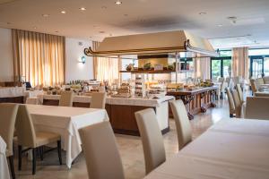 a restaurant with white tables and chairs and a kitchen at Hotel Excelsior in Lido di Jesolo