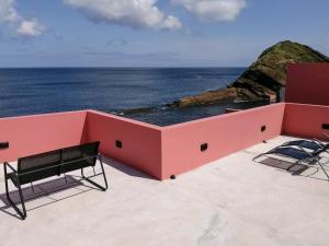 Terreiro Ocean House - Sea View في ساو روكي: مبنى وردي مع كرسيين والمحيط