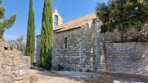 an old stone church with a tower and two trees at Le Petit Cocon in Vénéjan